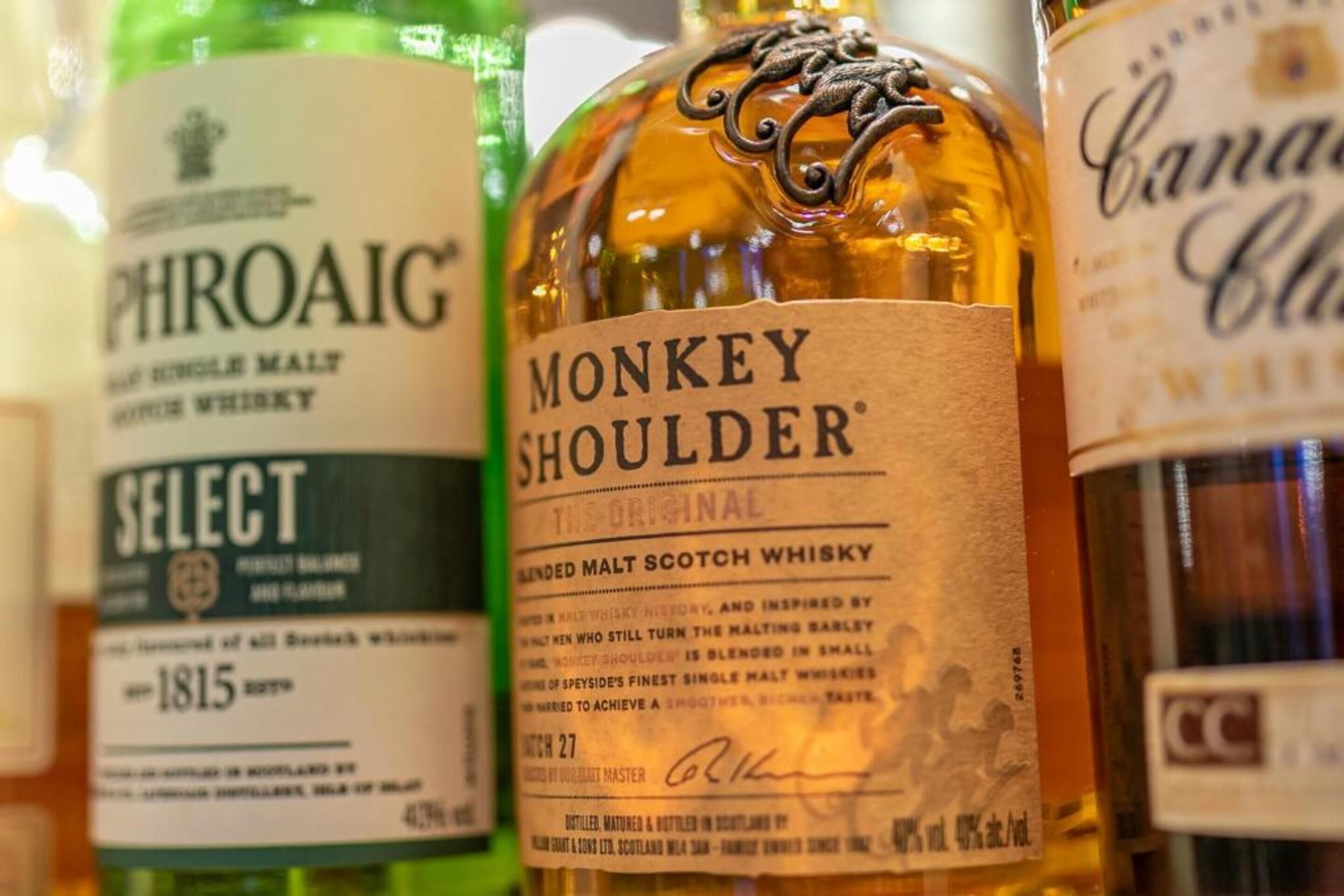 Uma seleção de garrafas de whisky, incluindo marcas como PHROAIG, MONKEY SHOULDER e CANADA CLUB.