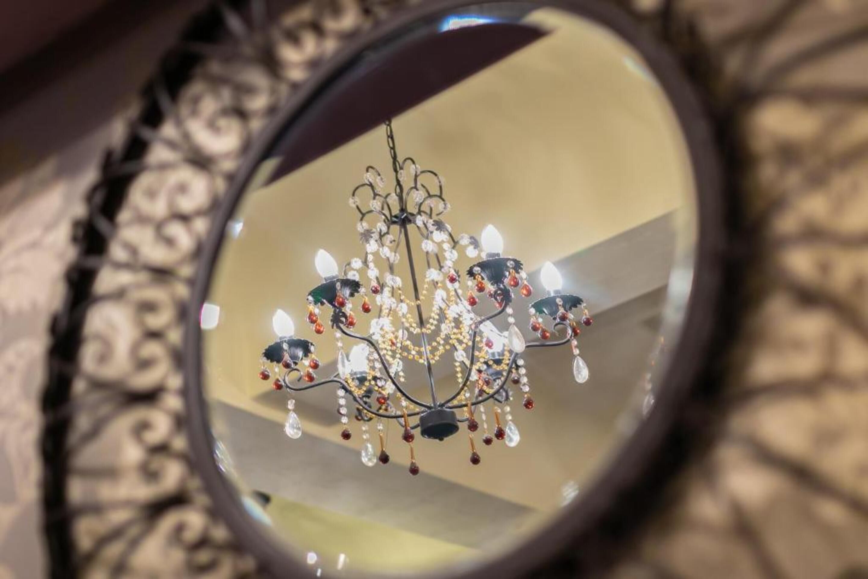 A chandelier with multiple arms and hanging crystals reflected in a round mirror.
