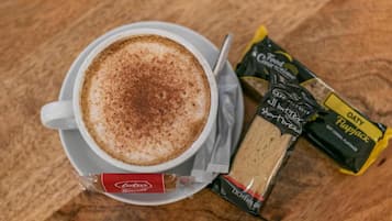 A cup of coffee with a frothy top, a packet of biscotti, and a packet of Oatly Flapjack.