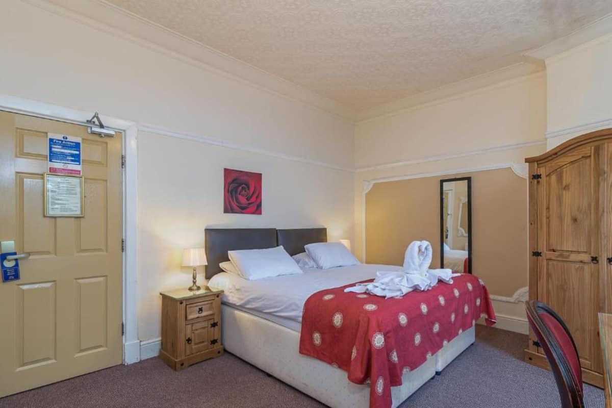 Une chambre d’hôtel comprenant un lit, une table de chevet, une armoire en bois et une porte munie d’un panneau indiquant les consignes de sécurité incendie.