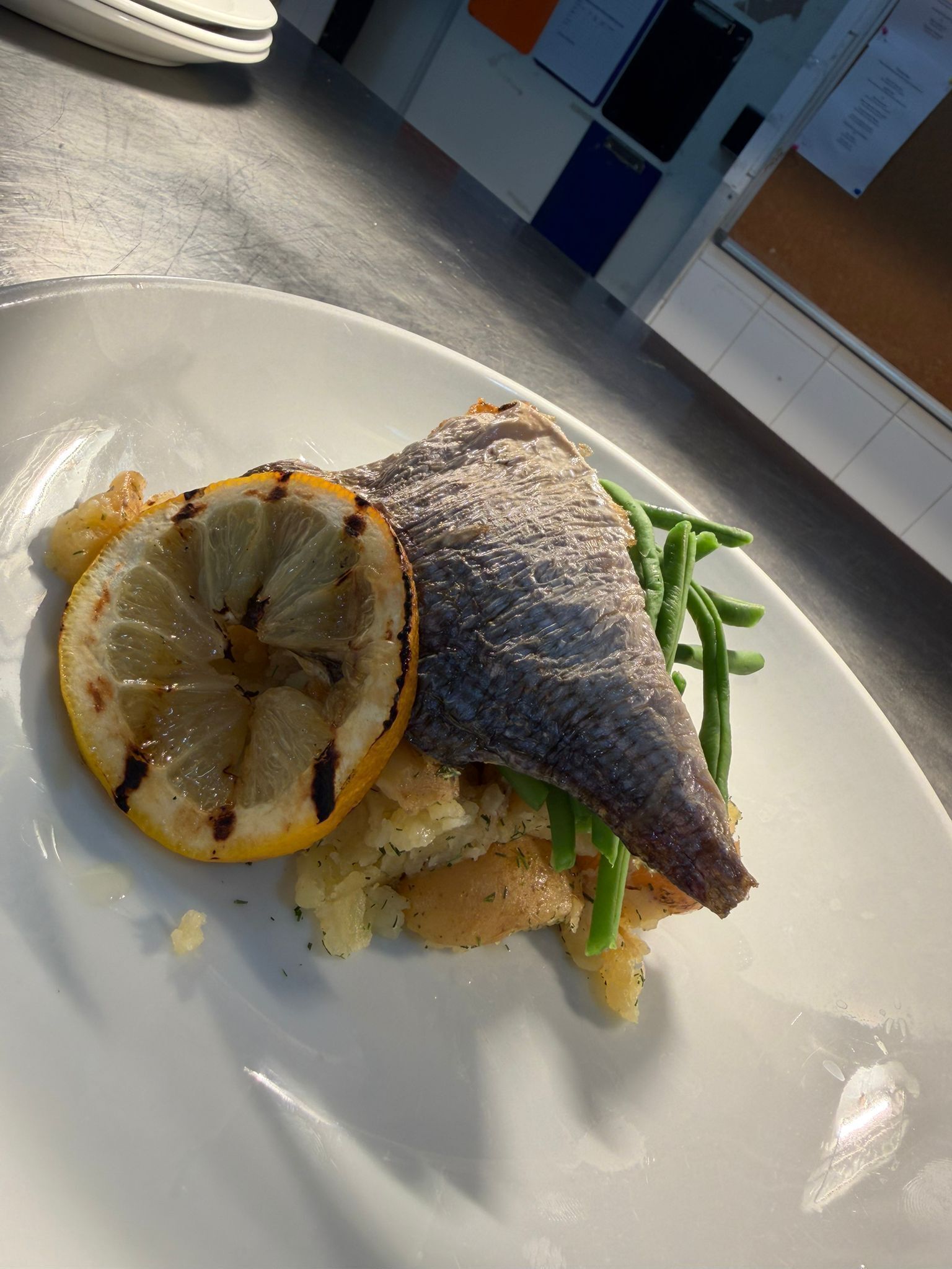 A plate with a fish, lemon slice, and green beans.
