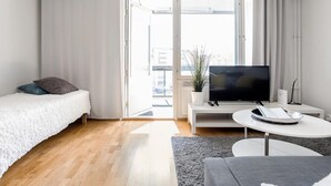 Ein modernes, helles Schlafzimmer mit einem Bett, einem Fernseher, einem kleinen weißen Tisch und einem grauen Sofa.