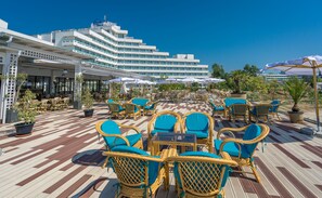 A rooftop terrace with wicker chairs and tables, a checkered floor, and a large building in the background. - Mera Onix Cap Aurora (Cap Aurora)