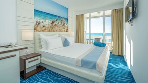 A hotel room with a large bed, a desk with a phone, a painting of a beach, and a TV on the wall. - Mera Onix Cap Aurora (Cap Aurora)