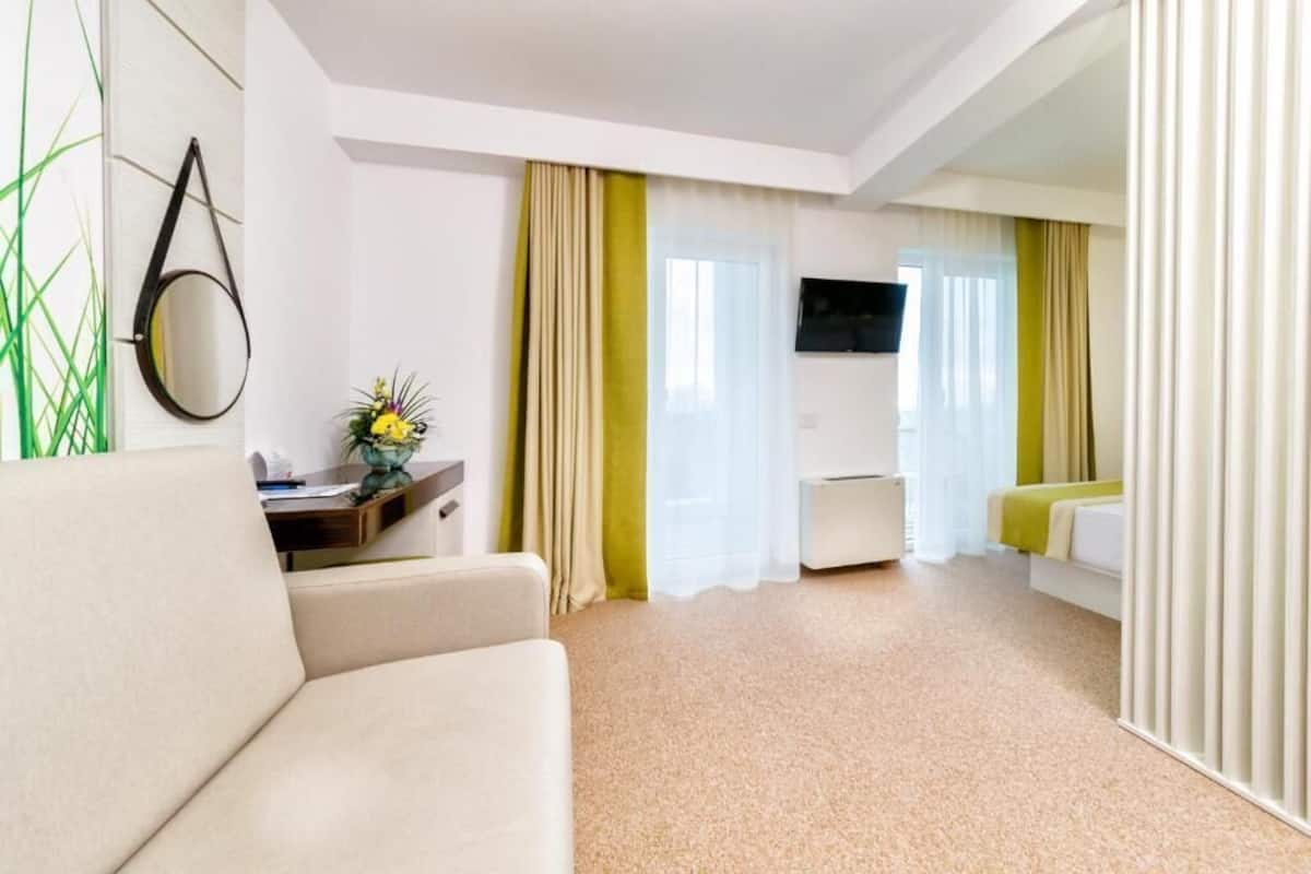 A hotel room with a sofa, a desk with a mirror, a TV, and a bed with curtains.