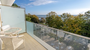 A balcony with glass railings, wicker furniture, and a view of the sea and trees. - Mera Brise (Mangalia)