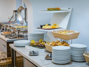 A buffet setup with various food items and stacked plates. - Mera Brise (Mangalia)