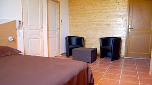 Una habitación con una cama, dos sillas, una mesita y una pared de madera.