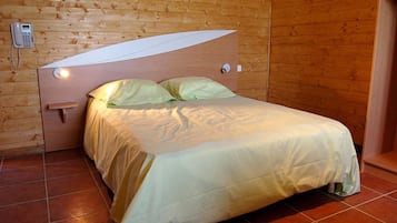 Un lit simple avec une tête de lit adossée à un mur en bois, un téléphone sur la table de chevet et une porte avec une poignée.