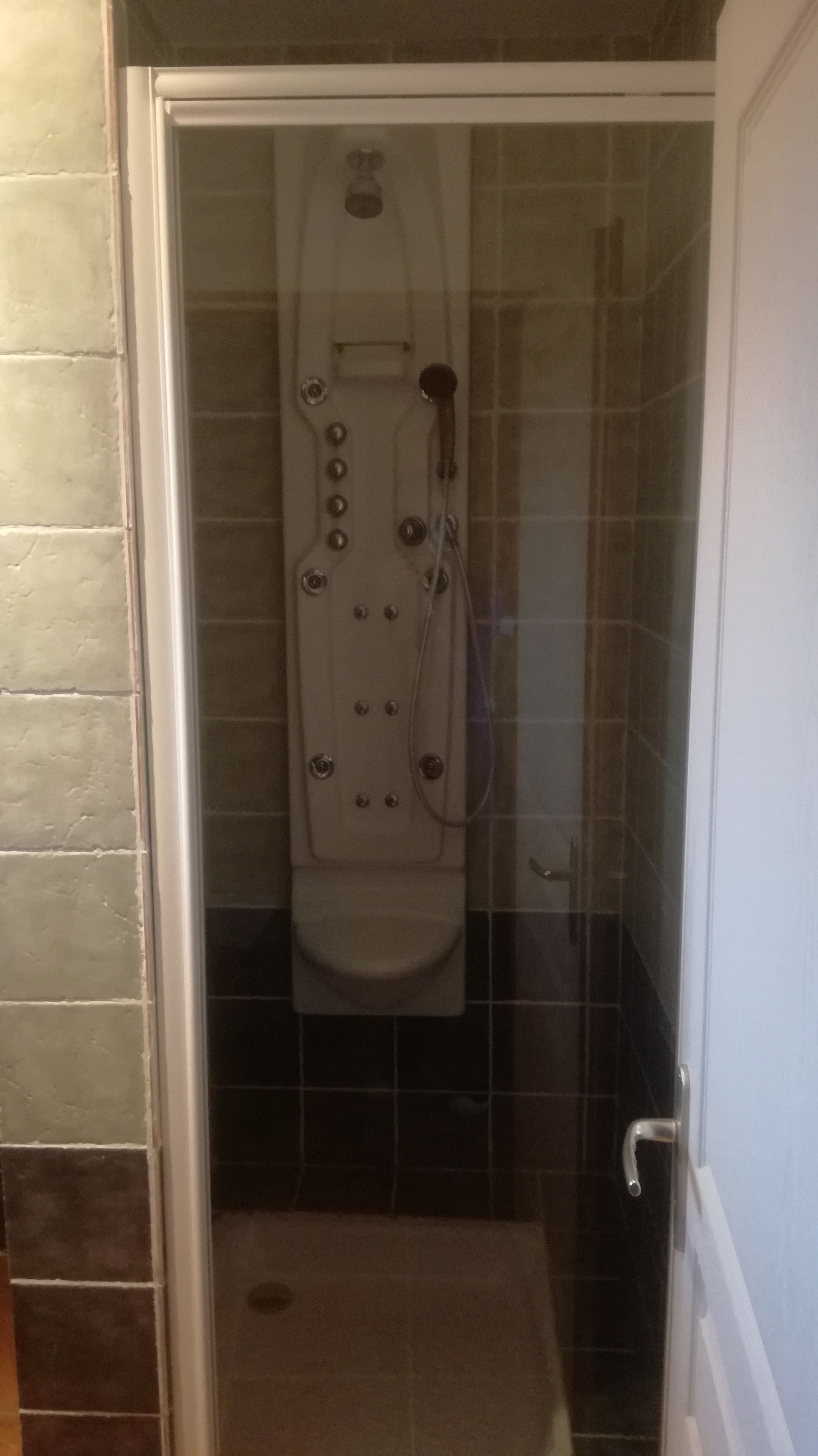 Cabina doccia con pareti in vetro, una vasca da bagno bianca, piastrelle e soffione visibile.