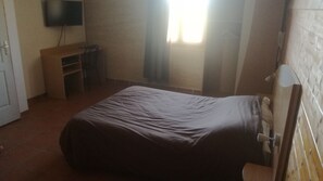 A bedroom with a bed, a desk, a chair, a television mounted on the wall, and a window with curtains. - Le Clos Boisé (Theziers)