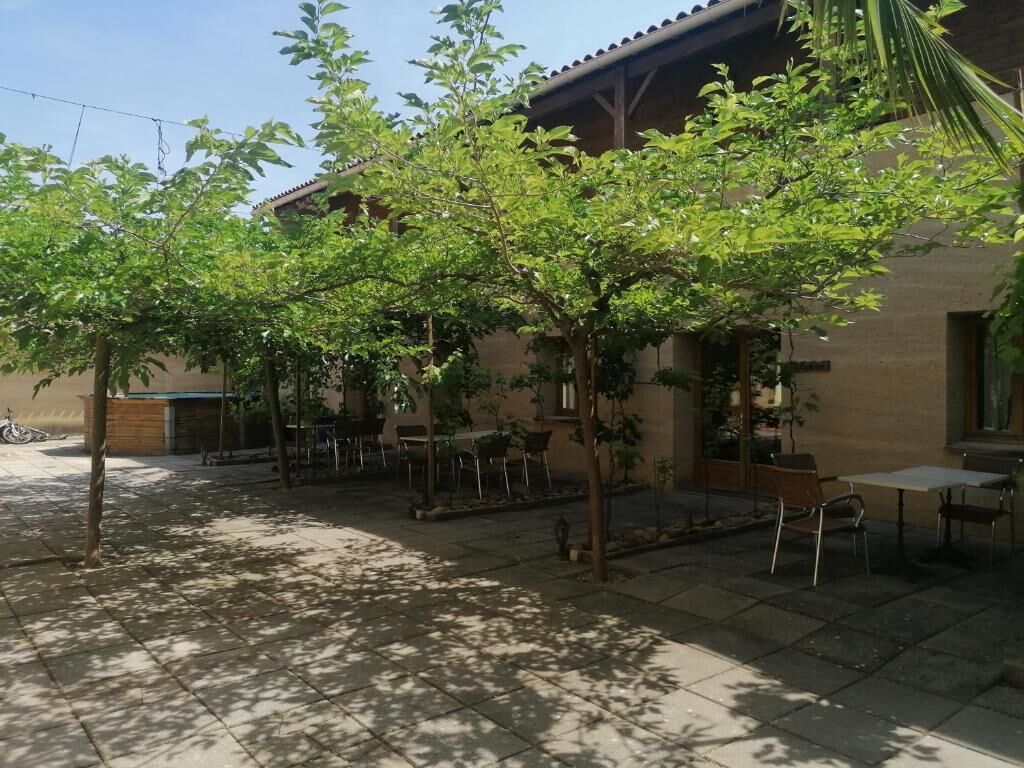 Un patio con zona de terraza, mobiliario exterior y un edificio con tejado de tejas.