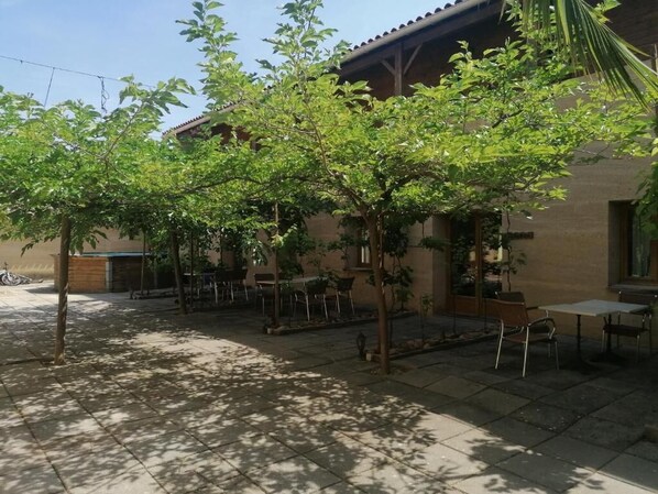 A courtyard with a patio area, outdoor seating, and a building with a tiled roof. - Le Clos Boisé (Theziers)