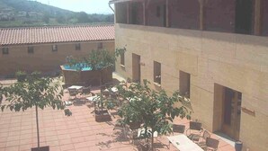 Un patio con mobiliario exterior, una piscina y un edificio con tejado de baldosas.