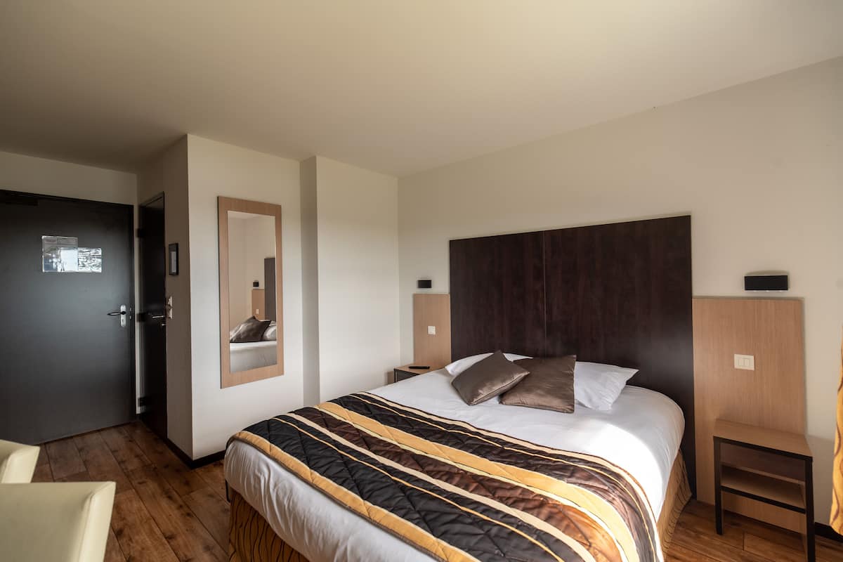 Ein Hotelzimmer mit einem großen Bett, einem Nachttisch, einem Sessel, einem Kleiderschrank und einem Spiegel.