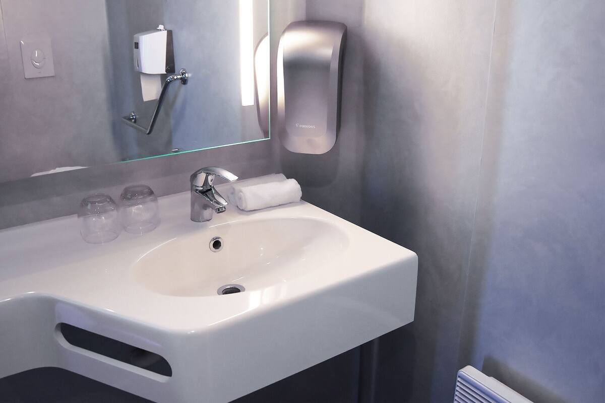 Ein modernes Badezimmer mit einem weißen Waschbecken, einem Spiegel, einer Seifenspender und einem Handtuch.