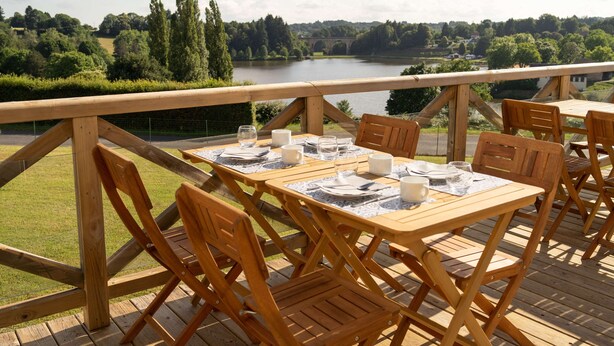 Een terras met houten tafels en stoelen, met uitzicht op een rivier en groen.