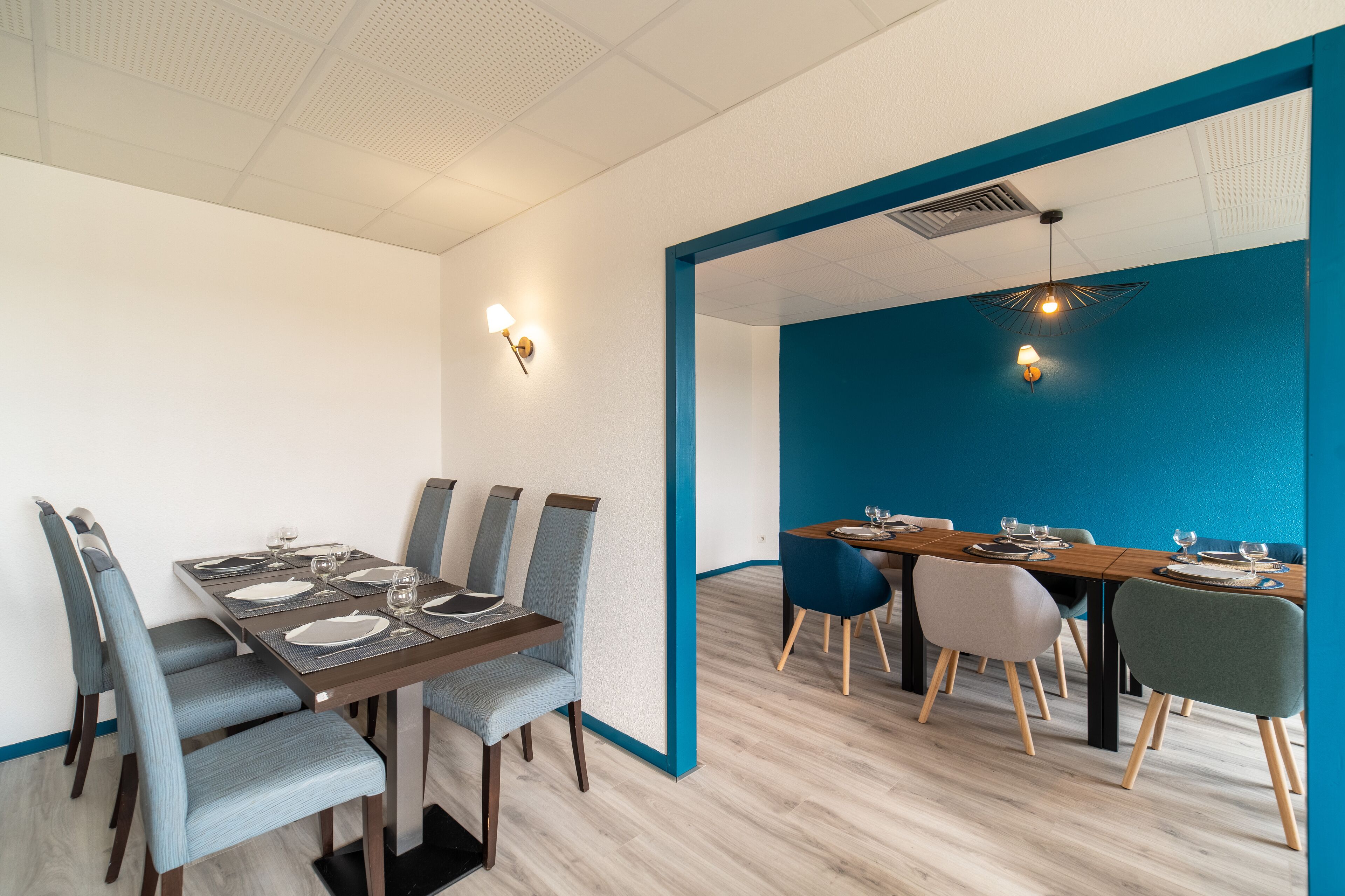 A dining area with a long table set for six, surrounded by chairs, and a blue accent wall.