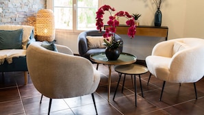 Een moderne woonkamer met een bakstenen muur, een groot raam en een open haard. Er staan twee fauteuils, een bank en een kleine ronde tafel met een bloevas.