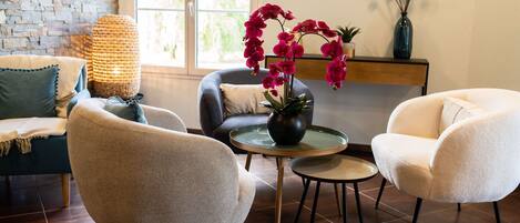 A modern living room with a brick wall, a large window, and a fireplace. There are two armchairs, a sofa, and a small round table with a vase of flowers.
