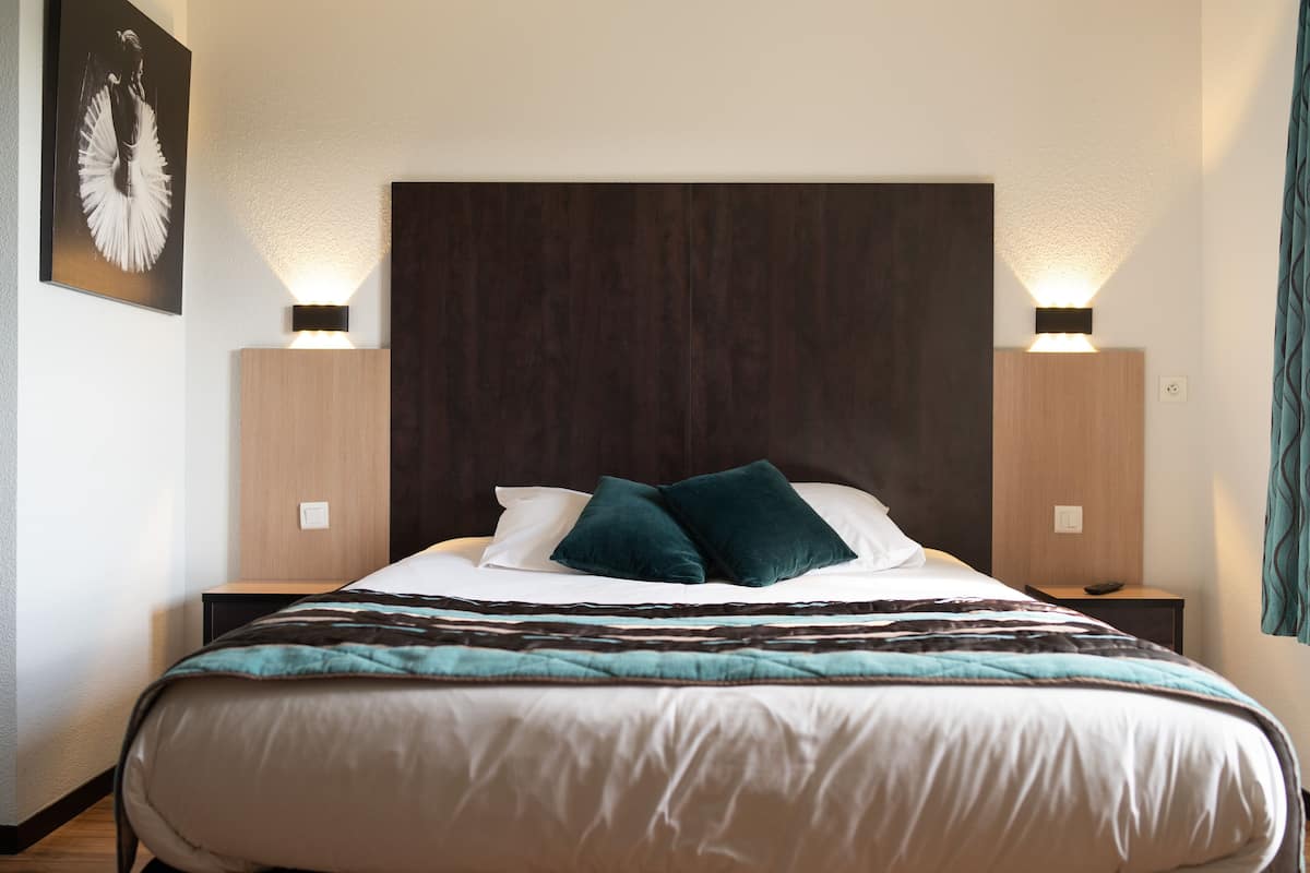 Ein ordentlich gemachtes Bett mit dunklem Kopfteil, zwei Nachttischlampen und einem gerahmten Bild an der Wand.