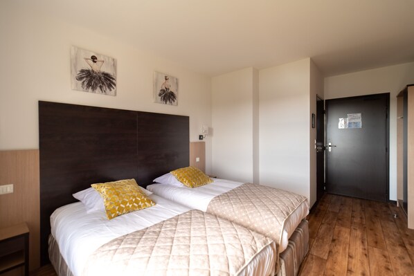 Habitación de hotel con dos camas, cabecero oscuro y cuadros en las paredes.
