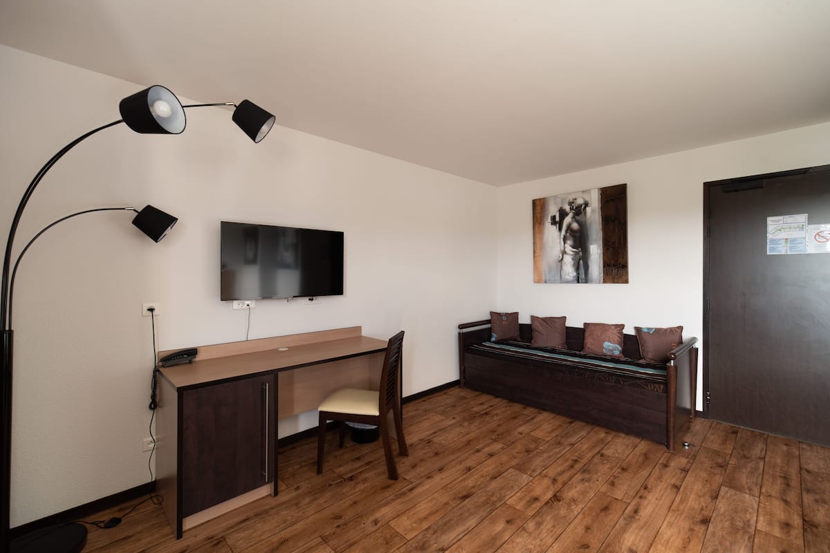 Ein Zimmer mit einem Holztisch, einem Stuhl, einem an der Wand befestigten Fernseher, einer Couch mit Kissen und einer Tür.