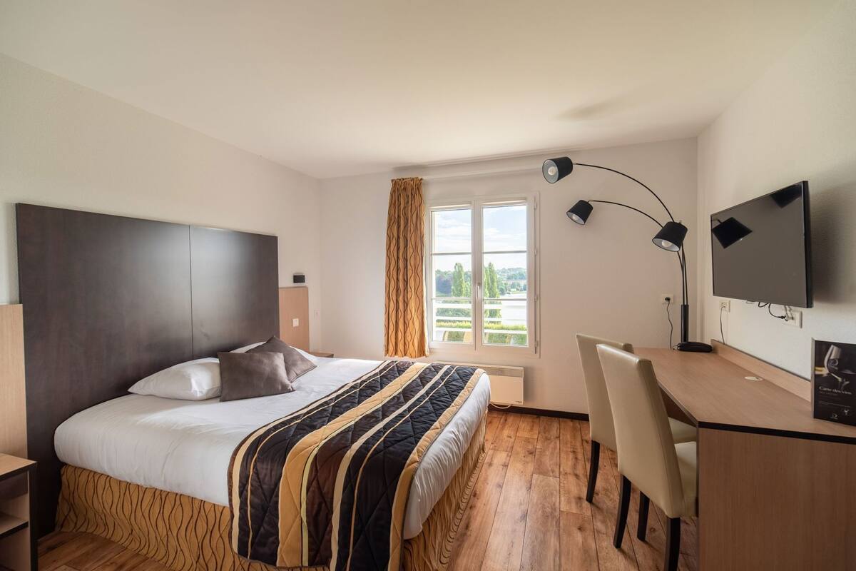 Ein Hotelzimmer mit Bett, Schreibtisch, Stuhl, Fernseher und einem Fenster mit Vorhängen.