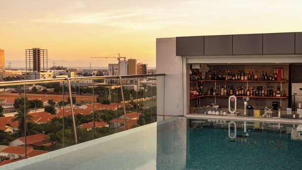 A rooftop infinity pool with a bar area and a city view.