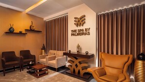 A modern spa room with a sofa, armchairs, a massage table, and a decorative wall with the spa's logo.