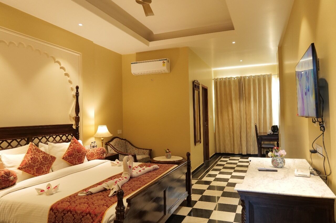 Habitación de hotel con piso a cuadros, cama con almohadas estampadas, mesita de noche con lámpara y televisor montado en la pared.