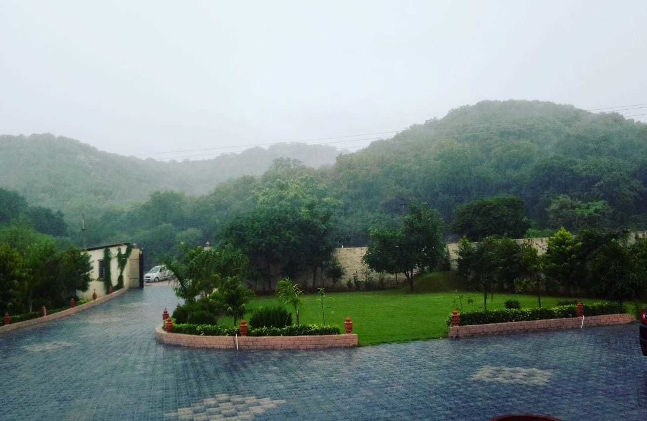 Un sendero pavimentado que lleva a la entrada de un edificio, rodeado de exuberante vegetación y un paisaje montañoso.