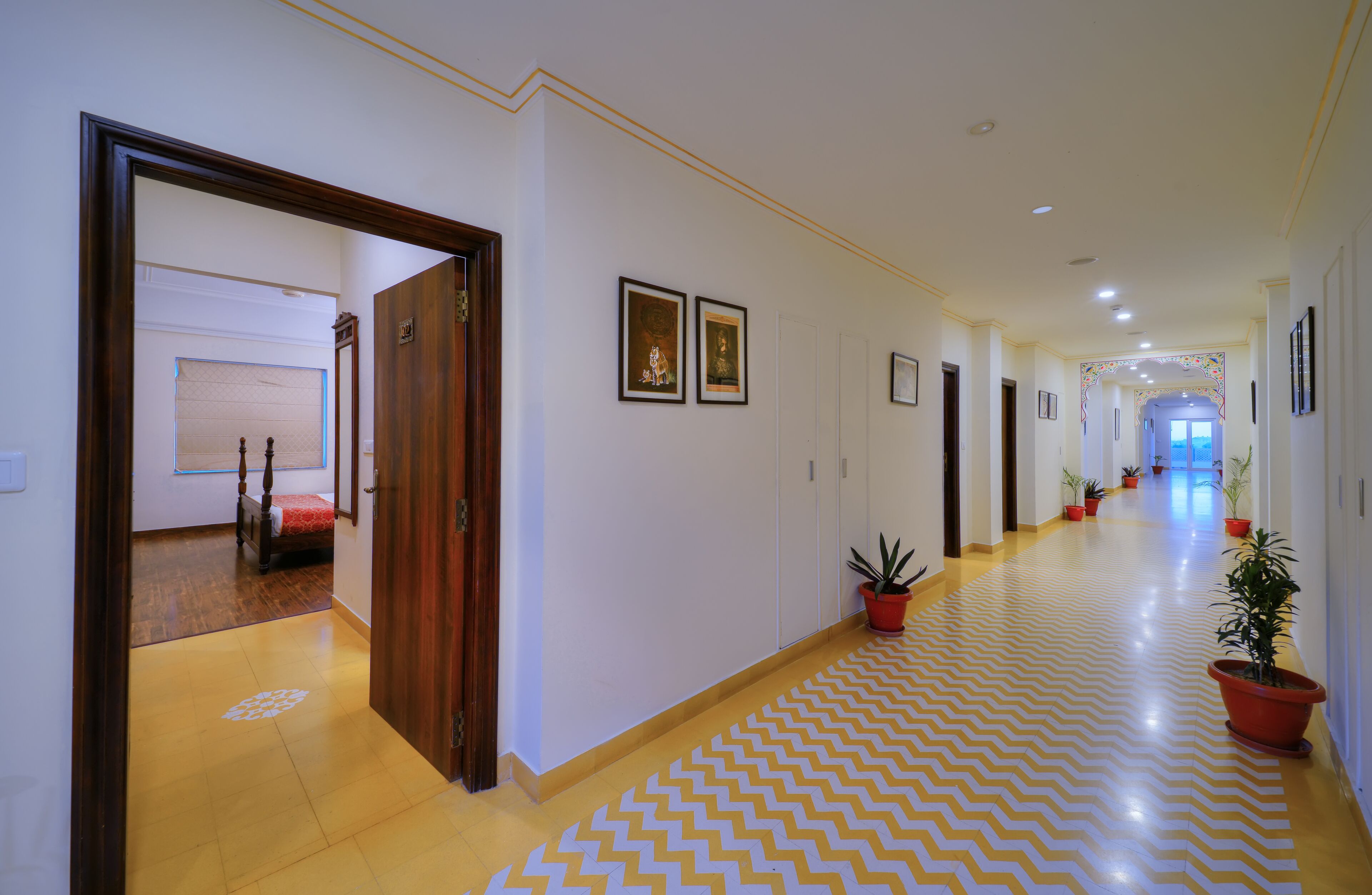 A hotel corridor with a patterned floor, wooden doors, and potted plants.