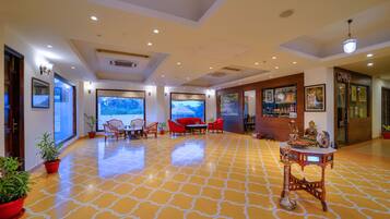 A spacious lobby with a patterned floor, seating area with red chairs, large windows with a view, and various wall decorations.