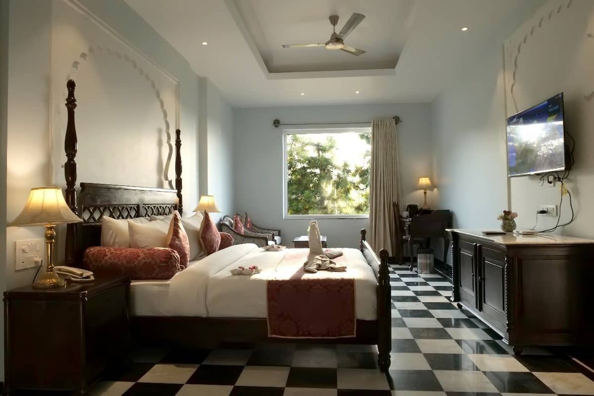 A hotel room with a bed, a desk, a television, and a window with a view of trees.