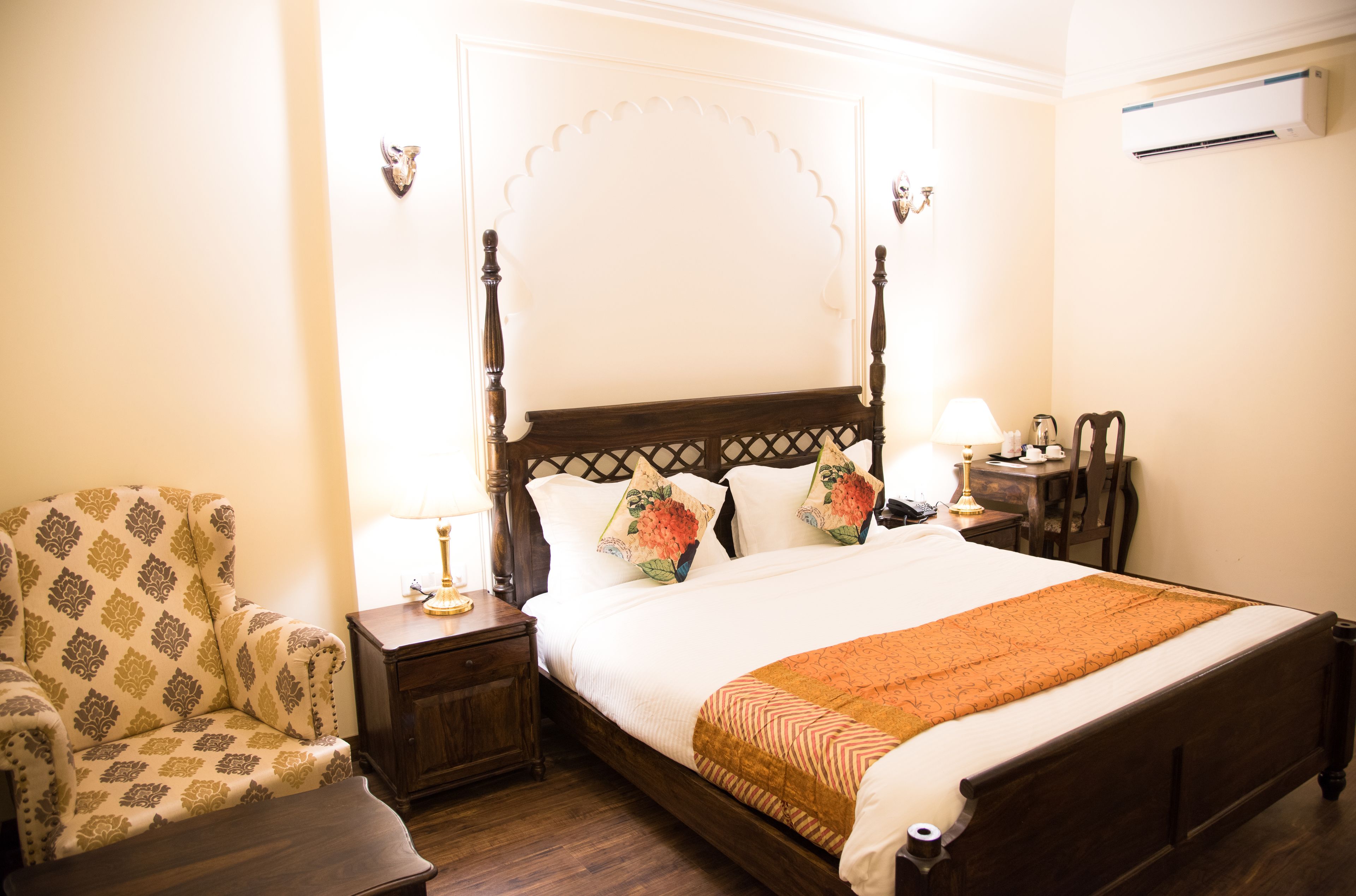 A bedroom with a four-poster bed, a nightstand, a chair, and a desk with a lamp.
