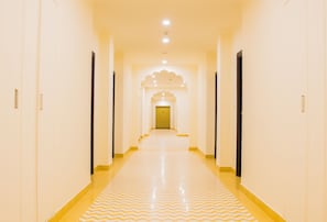 A long, narrow hallway with a patterned floor and doors on both sides leading to a room with a decorative archway. - WelcomHeritage Mount Valley Resort, Ranthambore (Sawai Madhopur)