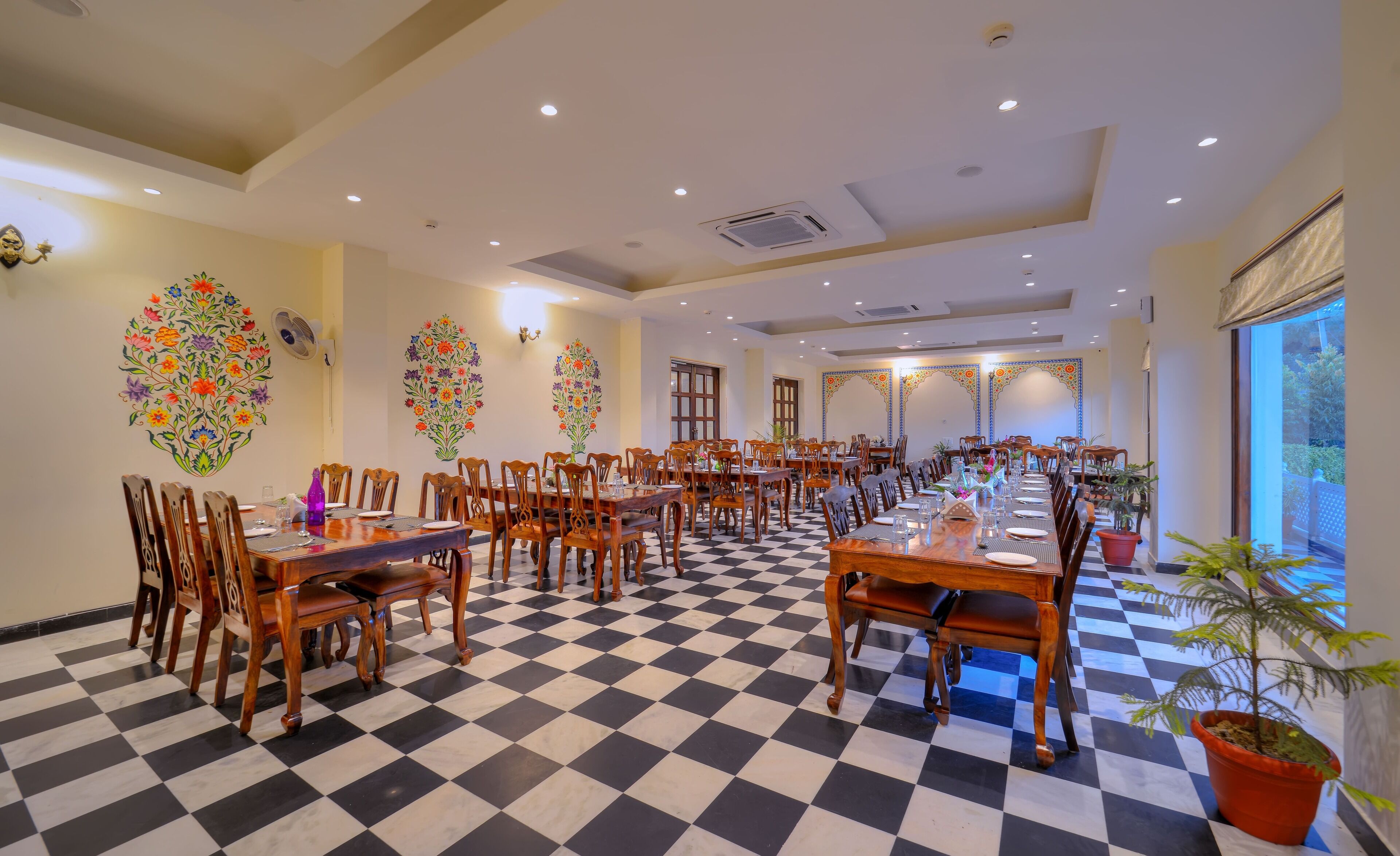 A spacious dining area with checkered flooring, wooden tables and chairs, and decorative floral wall art.