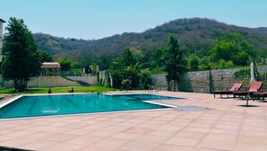 A swimming pool with a gazebo, lounge chairs, and a view of a forested hill. - WelcomHeritage Mount Valley Resort, Ranthambore (Sawai Madhopur)