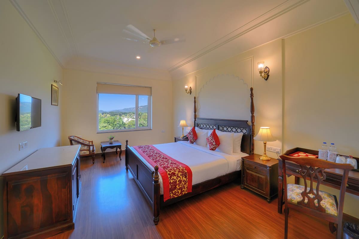 A hotel room with a large bed, a desk, a chair, a TV, a window with a view, and a ceiling fan.