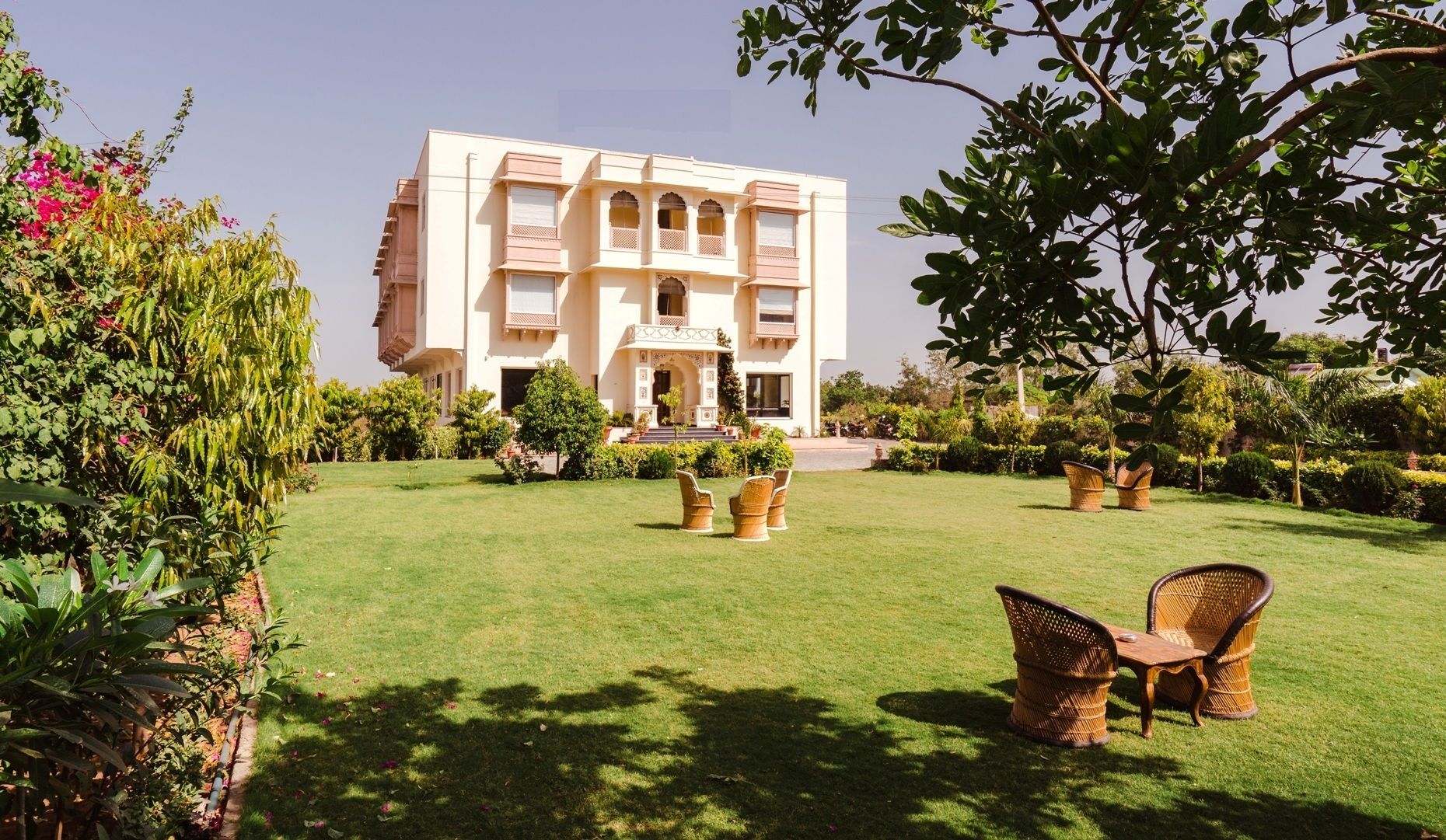 A large, multi-story building with a traditional architectural style, surrounded by a well-maintained garden with grass, shrubs, and a few trees.