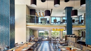 A spacious dining area with multiple tables and chairs, a checkered floor, and a view of the outdoors through large windows.