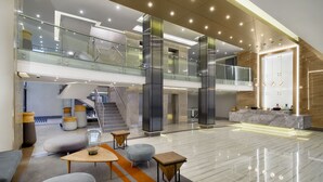 A spacious lobby with a high ceiling, a central staircase, and a reception desk.