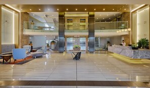 Eine großzügige Lobby mit Marmorboden, Sitzgelegenheiten, einer Rezeption und einer Treppe zu einer oberen Ebene.