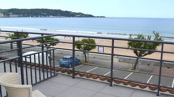 Un balcón con vista a la playa y al océano, un estacionamiento y una silla de mimbre.