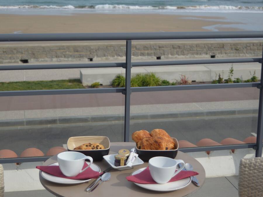 Una mesa en el balcón con vista a la playa y al océano.
