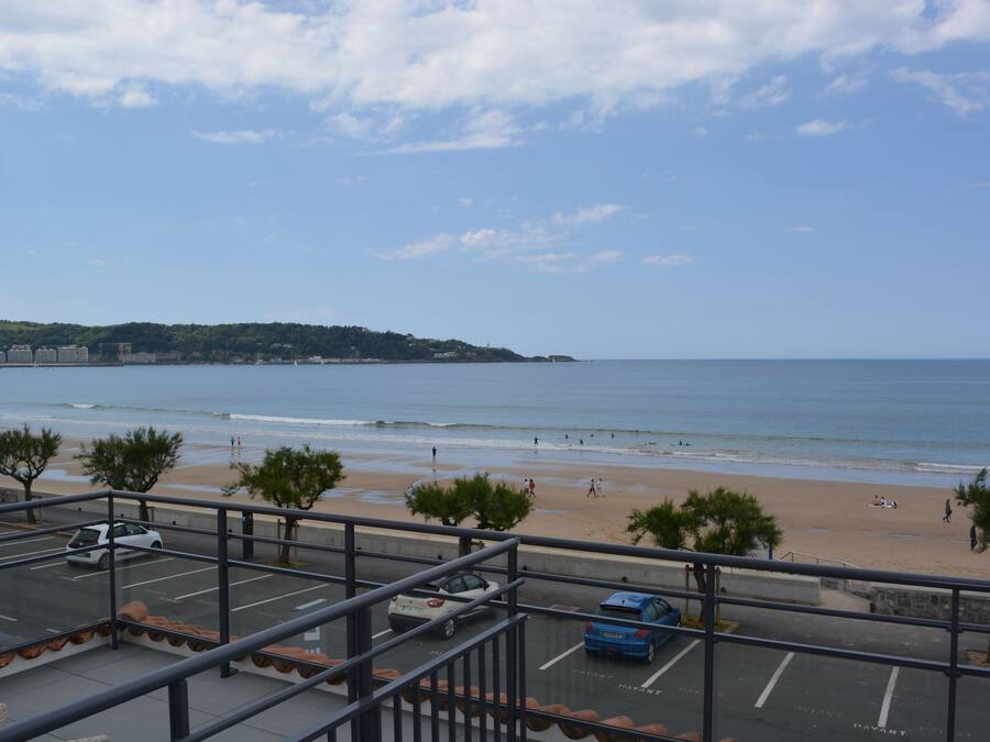 A parking area with cars, a beach, and a view of the ocean.
