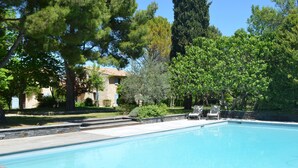 A swimming pool with a stone deck, surrounded by trees and a stone wall.
