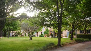 A courtyard with a lawn, trees, and buildings with stone walls and windows.