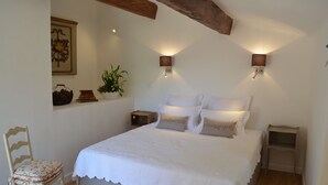 A bedroom with a large bed, two bedside tables, a chair, a wall-mounted plant, and a decorative wall piece.
